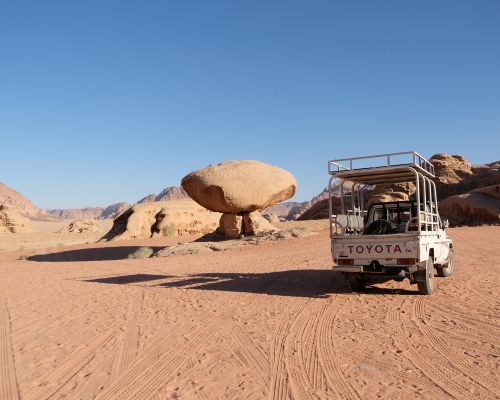Travelers enjoying a camel ride and jeep tour at sunset with Wadi Rum camp in the distance